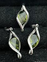 Photo of the pendant and matching earrings featuring green marquise-shaped faceted gemstones with silver-tone twisted metal frames.