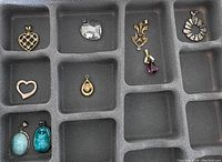 Top down image showing nine assorted necklace pendants in a black foam jewelry tray