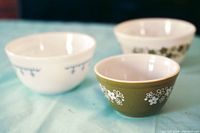Three vintage Pyrex mixing bowls on a turquoise surface, showing all floral and snowflake patterns clearly