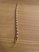 Photo showing the full tennis bracelet laid flat on a wooden surface, displaying alternating round clear and red stones set in gold-tone metal.