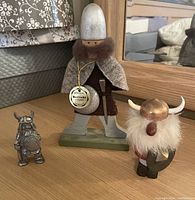 Photo showing three Viking figurines: a small pewter Viking, an original Sweden-made Butticki wooden Viking with tag, and a plush Viking with horns and shield.