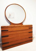 Front view of vintage teak dresser with attached large round mirror showing six drawers with black handles.