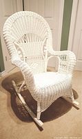 White wicker rocking chair placed indoors on carpeted floor against a green and white wall background