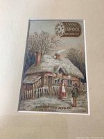 Close-up of framed card showing a cottage with thatch roof and two people outside, Eureka Silk advertisement.