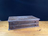 Front and top view of wooden antique spool cotton cabinet showing two drawers with knobs and labeled text.