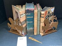 Books by Ayn Rand, Farrell, and Harrison standing upright between copper horse and rider bookends, with metal bookmark in front