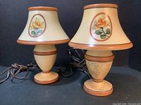 Pair of Bellova side table lamps with orange-trimmed cream bases and matching shades decorated with hand-painted roses, one base painted with lace/spiderweb design.
