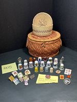 Full front image showing thimbles, pins, woven button boxes, sewing box against black background