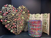Front view of Haitian metal heart tree, Indian wooden floral folding fence, and colorful woven basket set arranged against black backdrop.