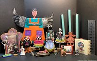 Wide view of the lot including terracotta skull candelabra, wooden angel figure with tin wings, various skeleton figurines including salt and pepper shakers, and themed artwork.