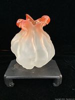 Front view of the frosted orange poppy bulb shaped art glass vase displayed on a black stand.