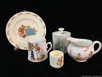 Five piece nursery ware set featuring Royal Doulton Bunnykins plate and tiny cup, Cat in the Fiddle creamer, Old Mother Hubbard mug, and Wedgwood Peter Rabbit jar with lid arranged together on black background.