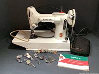 Singer sewing machine on black background with foot pedal, manual and extra presser feet in front