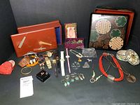 Overview photo showing a diverse collection of costume and sterling jewelry including watches, rings, earrings, and decorative boxes arranged on a black background.