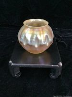 Bulbous fluted glass vase with iridescent pearlescent gold finish on a wooden stand