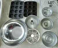 Overview of various aluminum and stainless steel bakeware including bunt pans, mixing bowl, and muffin tins on a light surface.