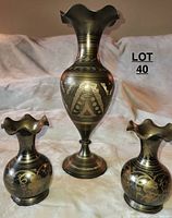 Set of three brass vases displayed on a fabric backdrop with medium and two small vases shown, emphasizing size contrast and etched designs