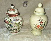 Two ceramic lidded vases side by side on fabric surface, one with colorful Japanese-inspired peacock motif, the other cream with floral design.
