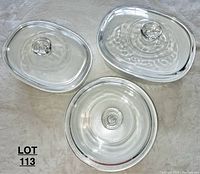 Three clear glass lids arranged on a soft surface, showing different shapes and knobs.
