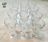 Set of 12 clear crystal wine glasses in a triangular arrangement on a cream surface, showing uniform cut diamond patterns on round bowls.