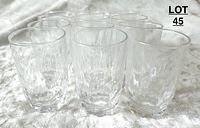 Photo showing 12 small clear glasses grouped and displayed on a fabric surface.