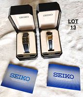 Pair of Seiko watches in original black and gold boxes with Seiko logo on inside lid, displayed on white fabric.