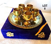 Set of six brass goblets arranged on brass tray on top of purple velvet box, showing front view of items with tarnish visible.