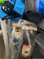 Two camping chairs packed or partially packed; one blue with mesh cup holder visible, one black in storage bag with label showing folding chair image.