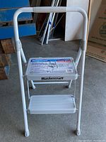 Front view of white metal two-step step stool with a handle, showing textured steps and frame.