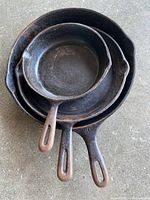 Photo showing three stacked cast iron skillets of different sizes with patina and use marks.