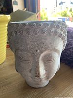 Gray pottery garden pot shaped as a peaceful face with curly hair detail.