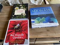 Three books arranged on a wooden surface showing covers of The Complete Language of Flowers, The Bee Friendly Garden, and The Ultimate Guide to Sea Glass.