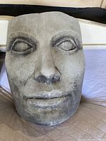 Close-up of the large light gray face sculpture, displaying detailed facial features with shadowed eyes.