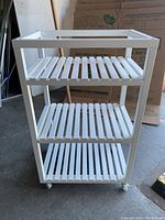 Front angled view showing all 3 white slatted shelves and casters beneath.