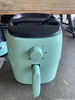 Front view of Dash air fryer in light green with timer dial and power cord on top