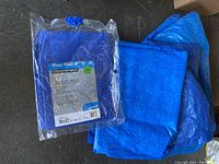 Four blue tarps shown, one sealed 10x12 tarp from LEAK brand, others folded on floor