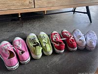 Photo showing four pairs of colorful low top Converse sneakers: pink, green, red, and white, all lined up on the floor; visible classic Converse design and labels