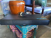 Black Onkyo Bluetooth surround sound speaker bar on a blue wooden table with a power adapter on top.