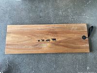 Long wooden charcuterie board with animal icons and attached leather loop