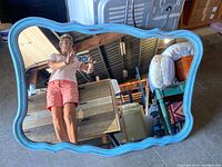 Front view of the large blue antique mirror showing wavy frame shape and clear glass reflecting person and surroundings.