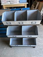Front view showing three tiers of bins; top tier with three compartments, middle and bottom tiers each with two compartments, all made of galvanized metal with handle and label holders.