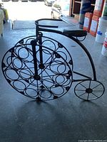 Side view of black metal wine rack designed as a vintage bicycle, showing detailed circular bottle holders on the front wheel and smaller rear wheel.