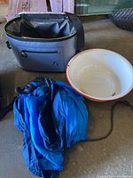 Photo of medium gray cooler bag, blue camping hammock folded, and white enamel metal wash basin