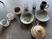 Overview of pottery mugs, dishes, mini casserole dish, and six ceramic mugs in wicker basket