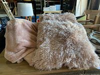 Soft pink faux fur blanket folded on a table with one side visible showing plush texture.