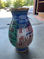 Front-side view of vase with painted scene of bridge, houses, trees on a blue background with gold trim.