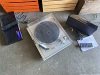 Photo showing record player with clear dust cover, adjacent to black DVD player and black audio system along with their remote controls.