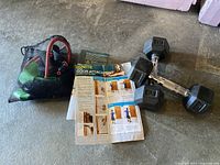 Photo showing two 8lb dumbbells, bungee cord set in a black mesh bag, and workout instruction pamphlets.
