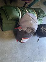 Two sleeping bags and one air mattress laid out on a concrete floor, showing the general size and color of each item.