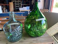 Photo showing both large glass vases side by side on a wooden surface in a workshop setting.